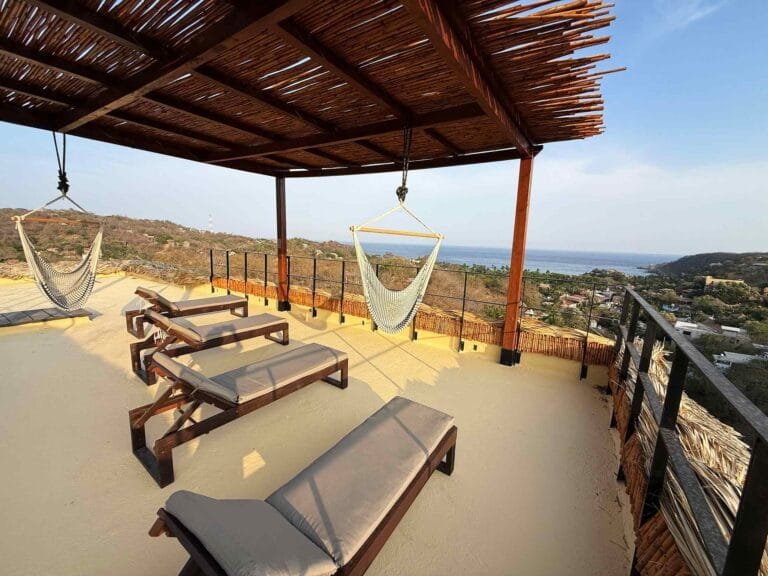 Pérgola de azotea con camastros y silla colgante frente al mar en Mazunte