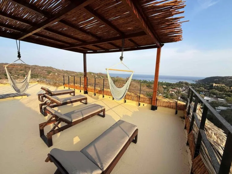 Pérgola de azotea con camastros y silla colgante frente al mar en Mazunte