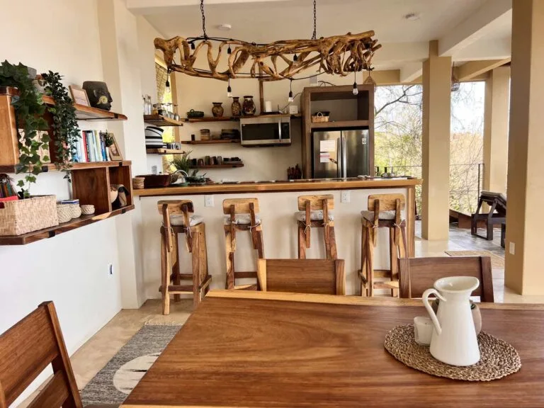 Comedor de madera con la cocina y el candelabro de madera flotada al fondo en Casa La Vista