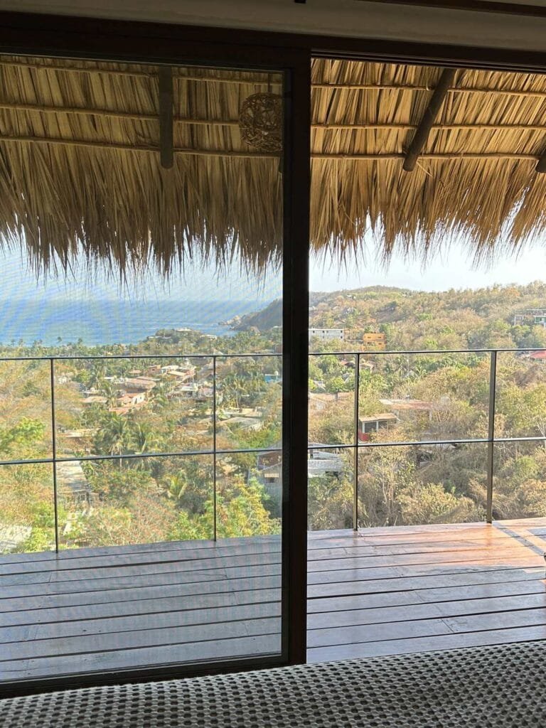 Vista a la bahía de Mazunte y al mar desde la cama de la Suite 1, a través de la puerta corredera al balcón privado