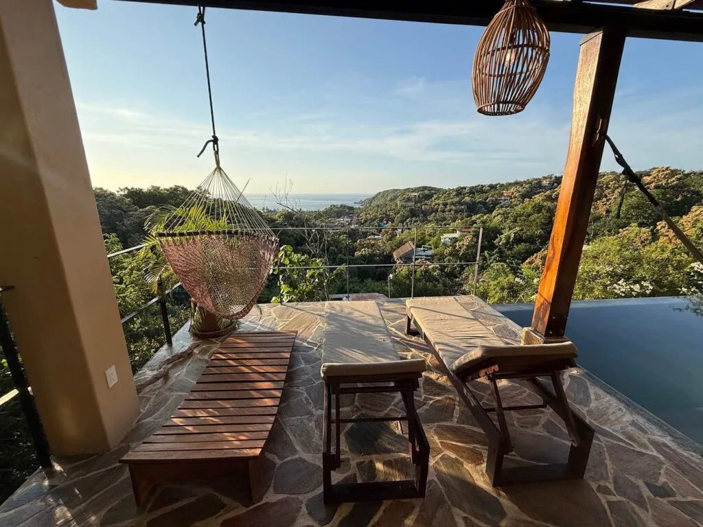 Terraza con camastros, banca de madera y silla colgante junto a la alberca en Casa La Vista